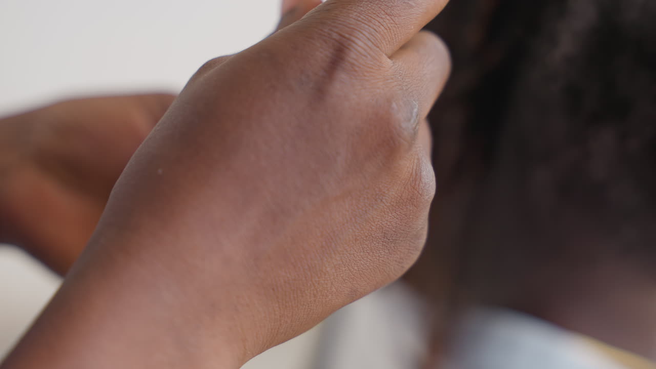 Closeup black hands combing braided hair, mother gently finishing small braids with yellow comb, indoor neutral background, textured afro hair, nurturing domestic moment focused on hands and scalp