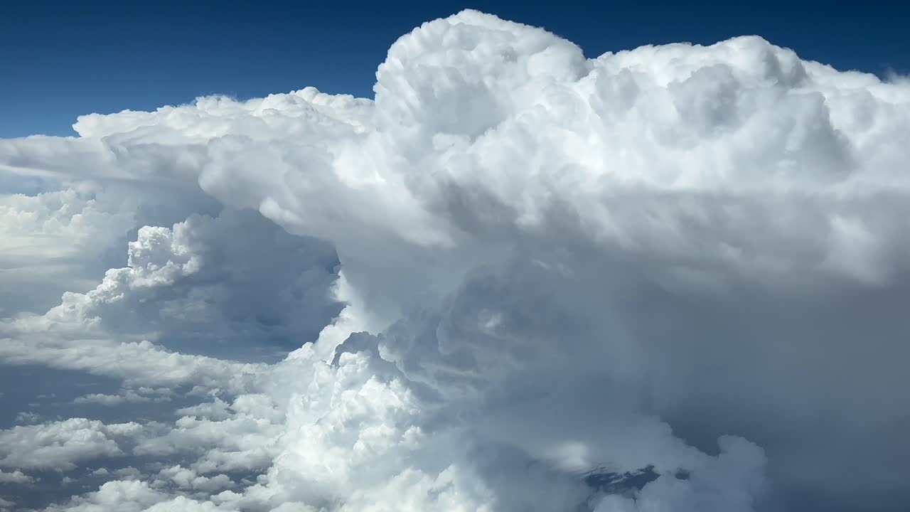 Pilot POV flying through a sky full of massive storm clouds. Aerial footage recorded from a jet cockpit. Daylight with an intense blue sky. 4K