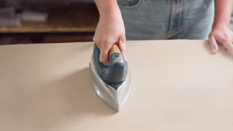 hand view of hand holding pressing iron, moving it round fabric surface, ensuring neat lines, focusing on precise motion, demonstrating skillful technique, enhancing garment presentation