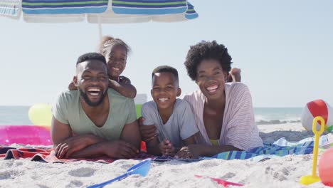 video of happy african american family lying on beach and laughing