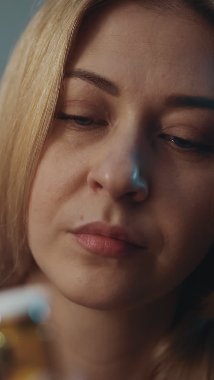 Thoughtful lady looks with suspect at small drug bottle with unregistered nutritional product on blurred background in semi-dark room closeup slow motion