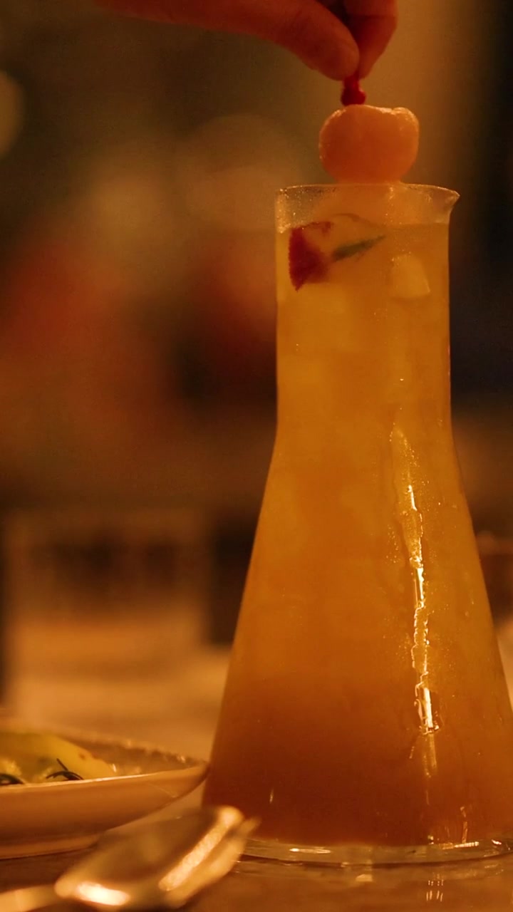 Una mano posiziona con cura una guarnizione di litchi sopra un cocktail alto e freddo in un bar.