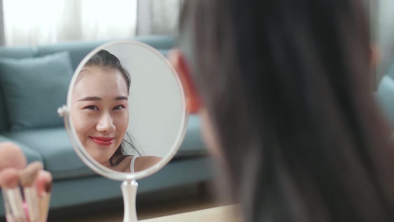 거울에서 반사 아름다운 젊은 아시아 여성은 그녀의 얼굴을 만지고 집에서 메이크업 적용 후 미소