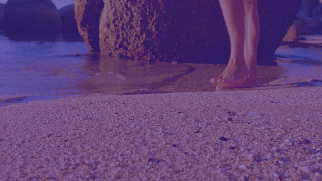 Walking barefoot on pebbled beach near large rock formation, enjoying scenery