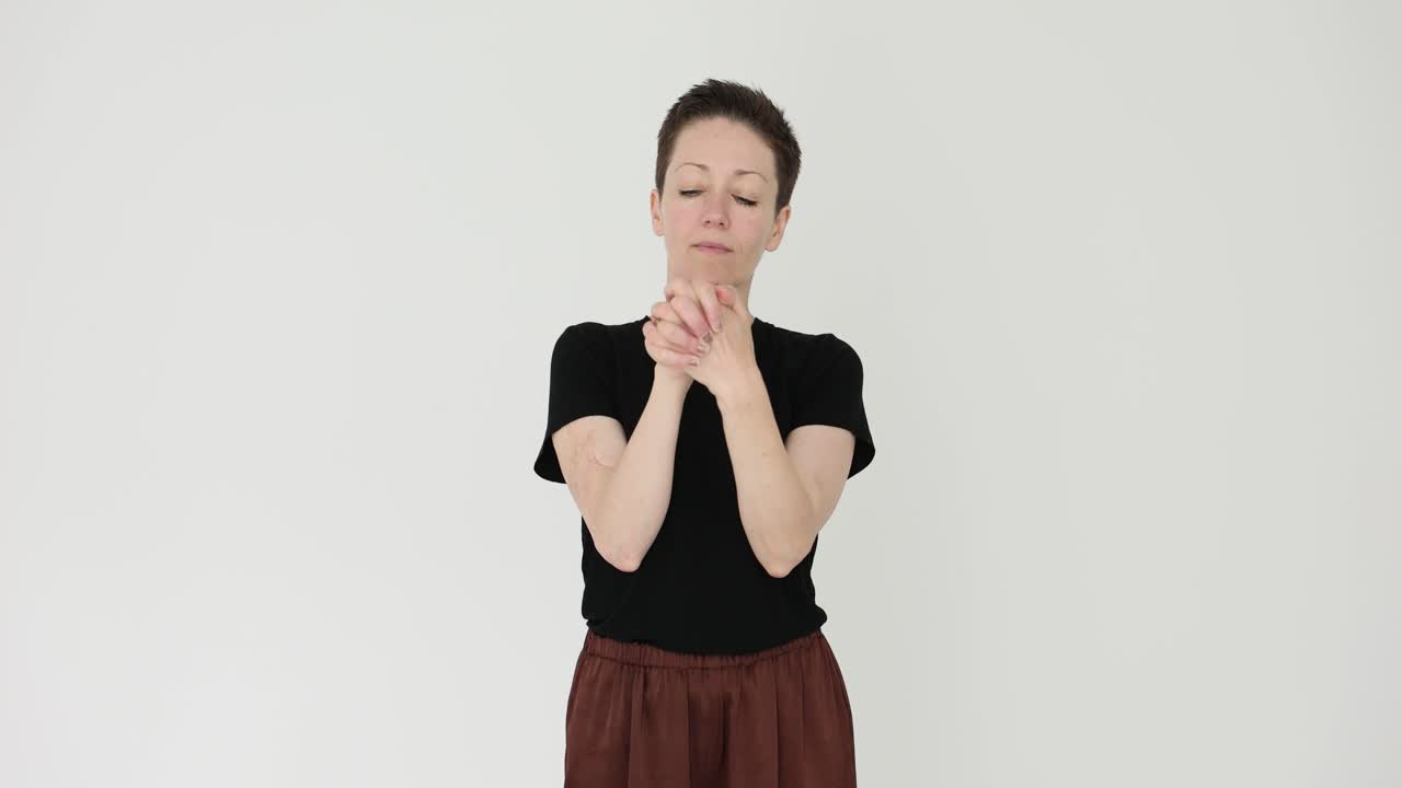 A woman rubs her hands together against a white background