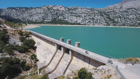 imágenes aéreas en 4k de dos conductores de scooter conduciendo sobre una presa de agua dulce en mallorca - turistas en españa, mallorca - presa de cuber - alquiler de scooter