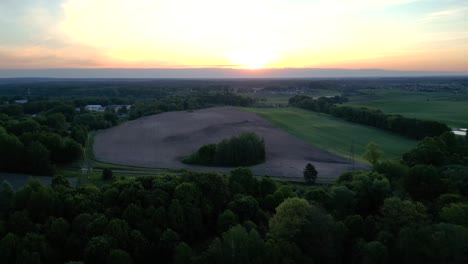 panorama al atardecer, vista de un paisaje con un bosque, campos y el sol poniéndose