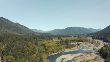 Gorgeous-aerial-drone-shot-of-a-blue-mountain-river-cutting-across-a-sandy-beach-floor