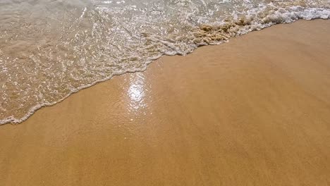 Waves gently wash over the sandy beach in Phuket, Thailand, under bright sunlight, creating a serene and calming atmosphere
