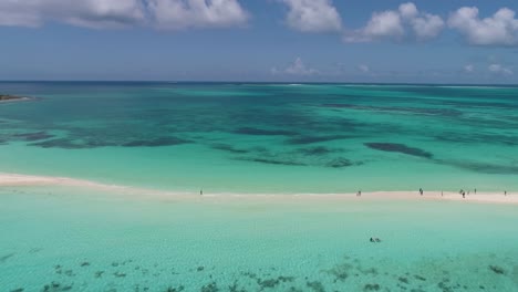 Drone-shot-people-walking-along-tropical-sandbar-with-crystal-clear-sea-water,-pan-left