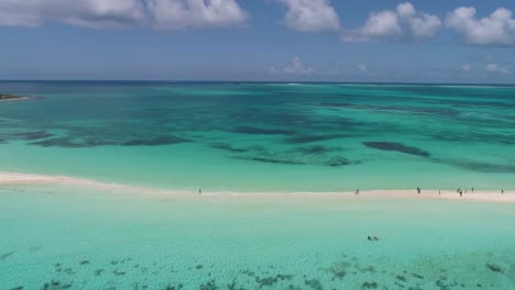 drone shot people walking along tropical sandbar with crystal clear sea water, pan left