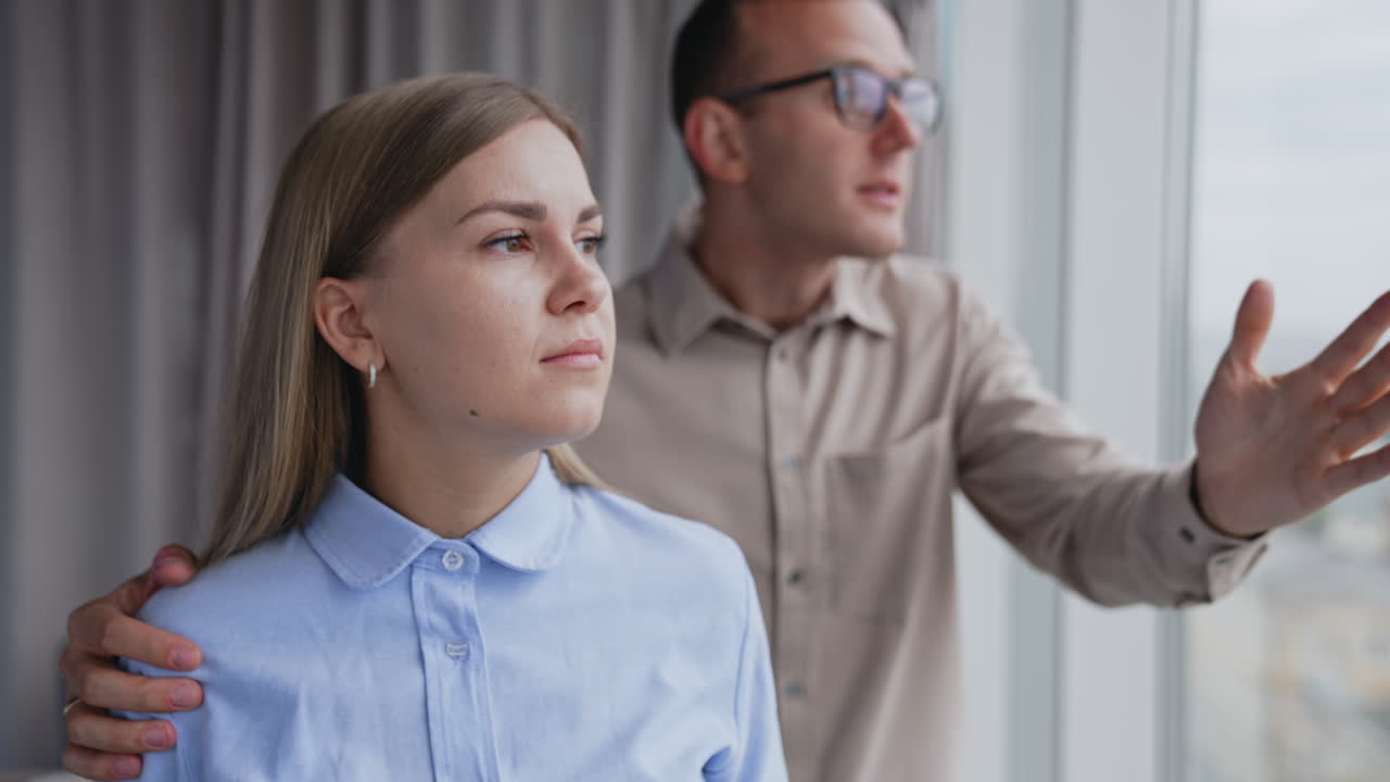 Young lady having headache and feels tired. Male colleague tries to comfort her and distract her pointing at window.