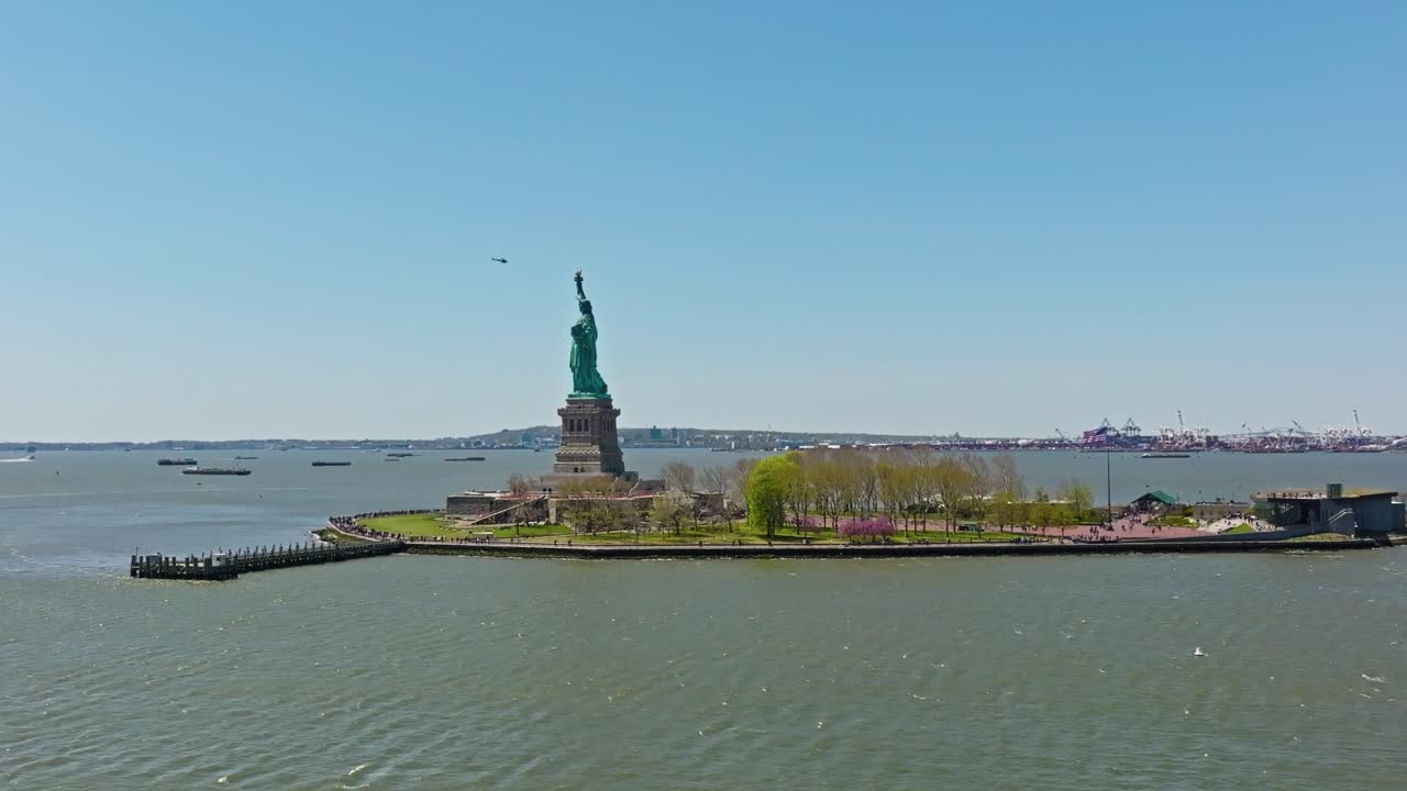 Aerial orbiting shot showing Statue of Livery on island and flying helicopter in background against blue sky - New York city, USA