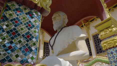 big statue of a monk sitting in meditative position at thai temple, panning shot low angle view