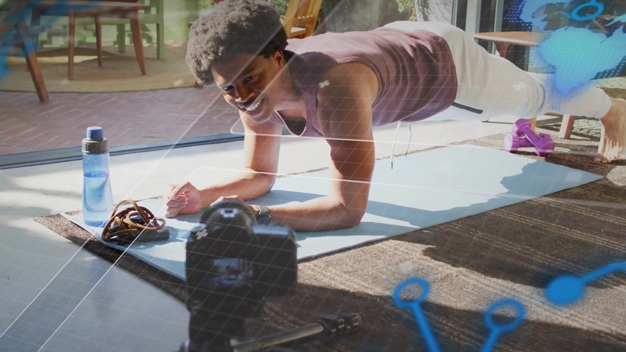Man holding forearm plank on mat, glancing at tripod camera, tightening core and recording fitness