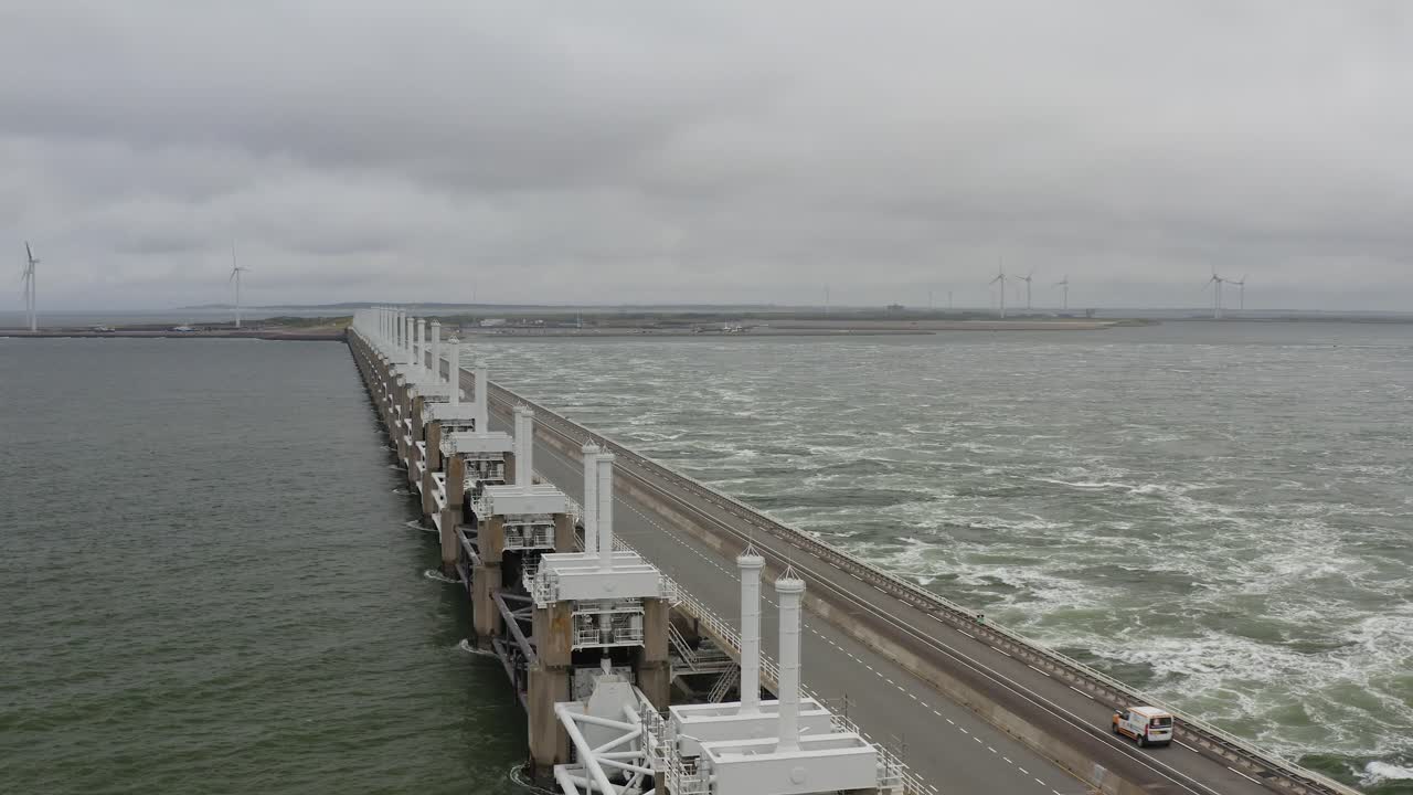 폭풍우 치는 날 네덜란드 zeeland에 있는 동부 scheldt 폭풍 해일 장벽 위로 운전하는 자동차의 공중 추적 샷
