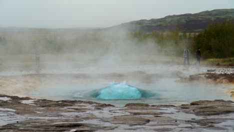 gente caminando por el géiser strokkur en erupción en el área geotérmica de islandia