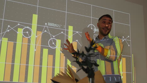 Male-Teacher-Giving-Maths-Or-Science-Lesson-In-School-Standing-At-The-Front-Of-Class-With-Projection-Of-Graph