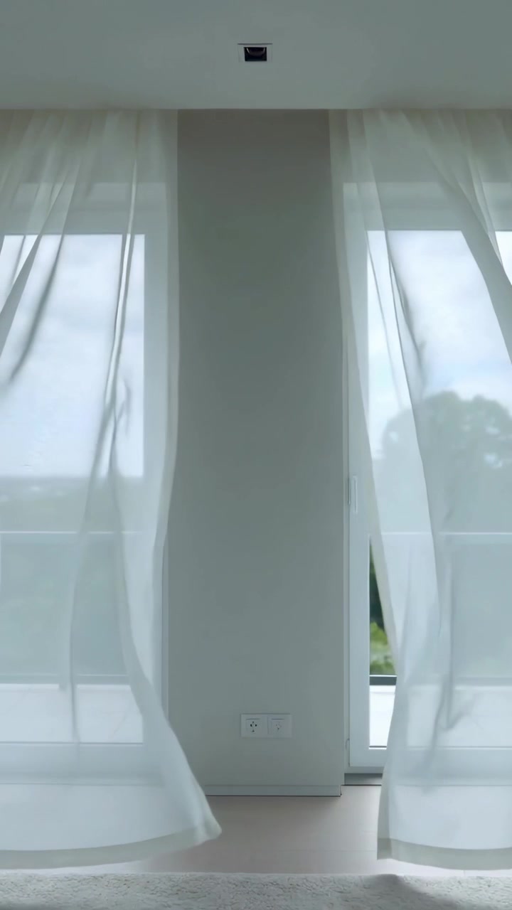 Vídeo vertical: Cortinas transparentes esvoaçantes balançando com a passagem de uma rajada de vento pelas portas da varanda em casa.