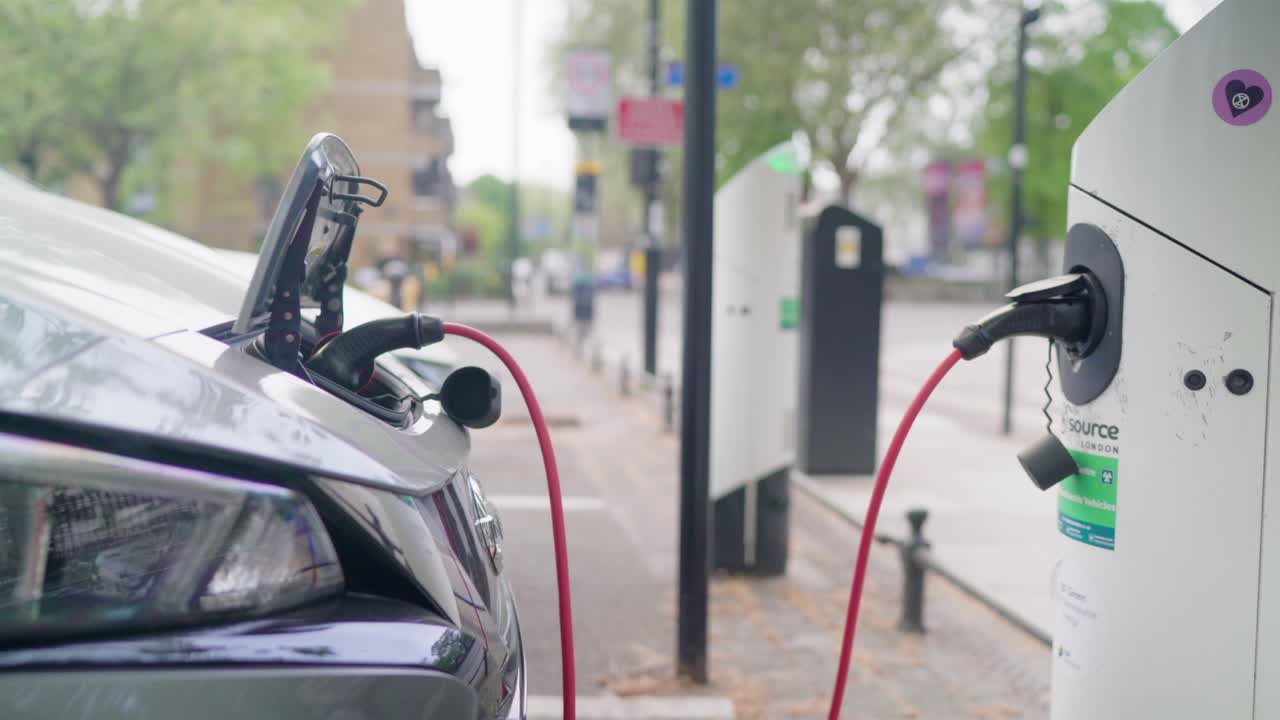 Kırmızı bir kabloyla otomobilin ön tarafına bağlanan bir şarj istasyonundan şarj edilen elektrikli hibrit araba