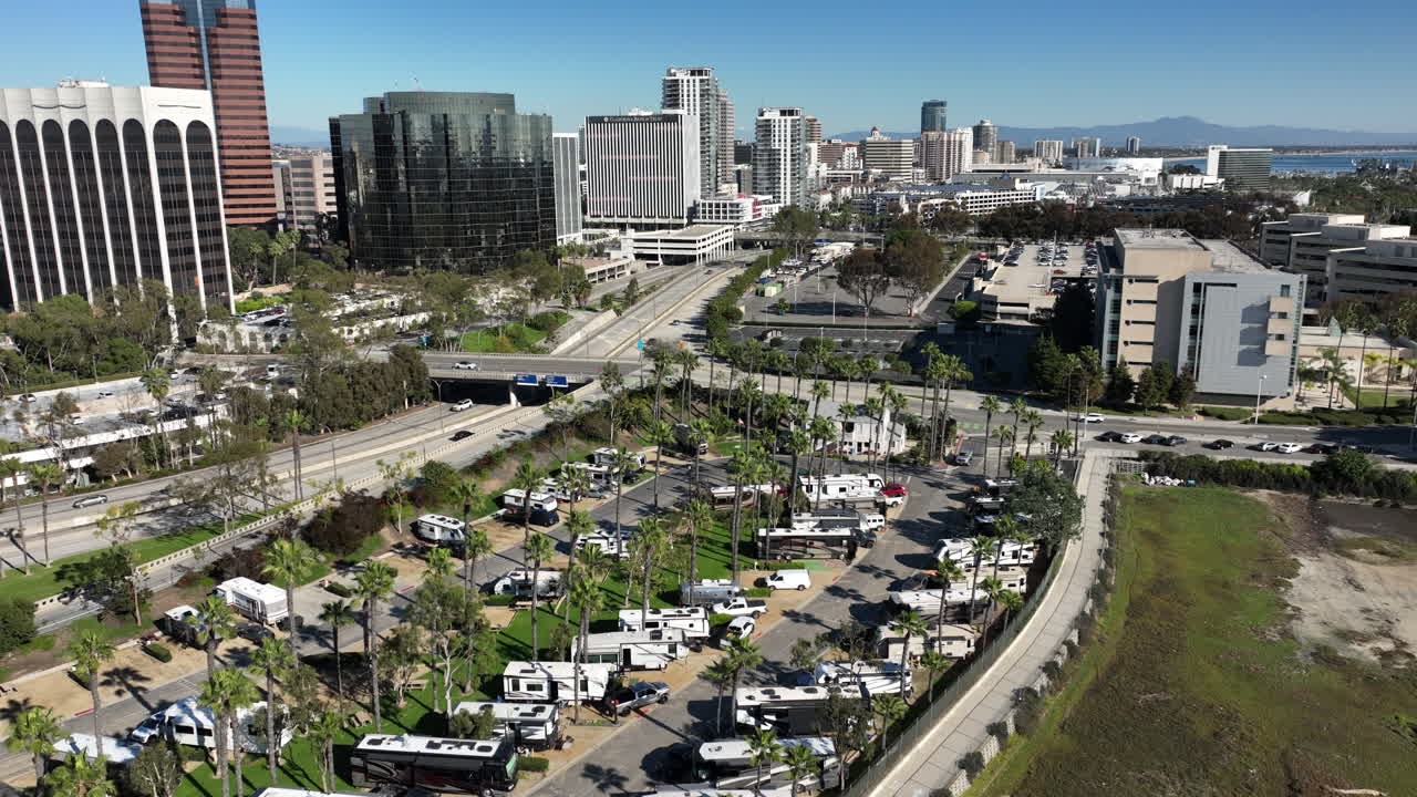 Vista aérea do centro de Long Beach, Califórnia, ao longo da Shoreline Drive em direção ao Pike Outlets e ao horizonte circundante em um dia ensolarado. A câmera se move para trás, revelando ruas costeiras.