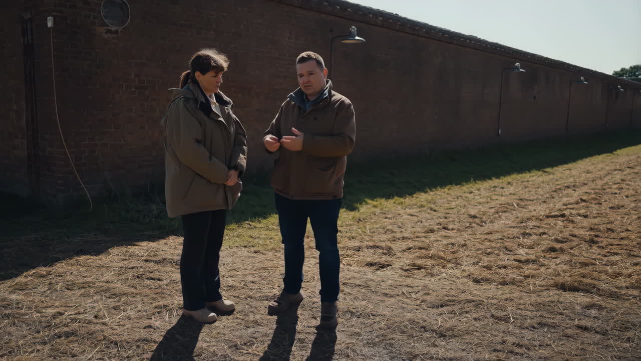 Two people having a discussion outdoors in front of a brick wall