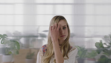 portrait of beautiful young blonde woman intern looking at camera running hand through hair in office workspace background