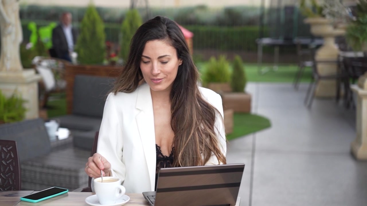 Una joven teletrabajando en una acogedora cafetería al aire libre utilizando una tableta para sus tareas