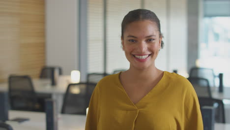 Portrait-Of-Smiling-Young-Businesswoman-Walking-Into-Focus-In-Modern-Open-Plan-Office