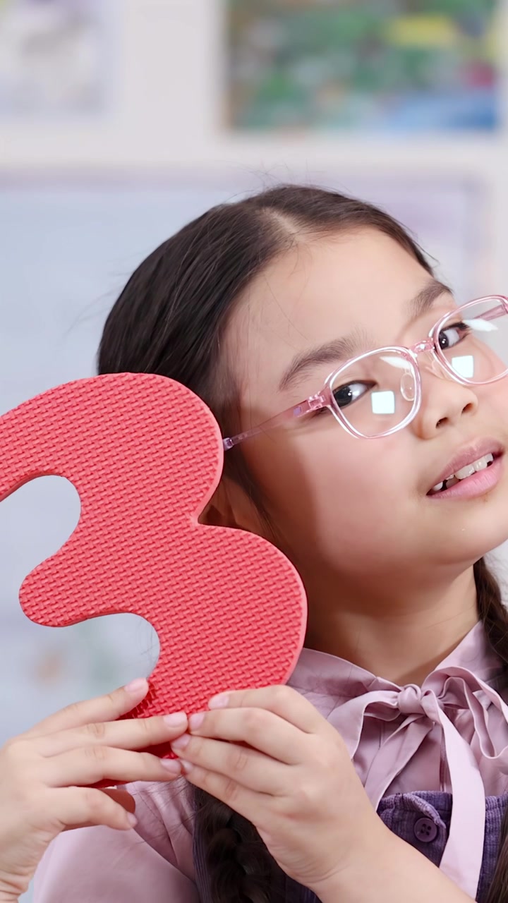 Una bambina con gli occhiali tiene in mano un numero tre rosso durante un'attività di matematica in classe.