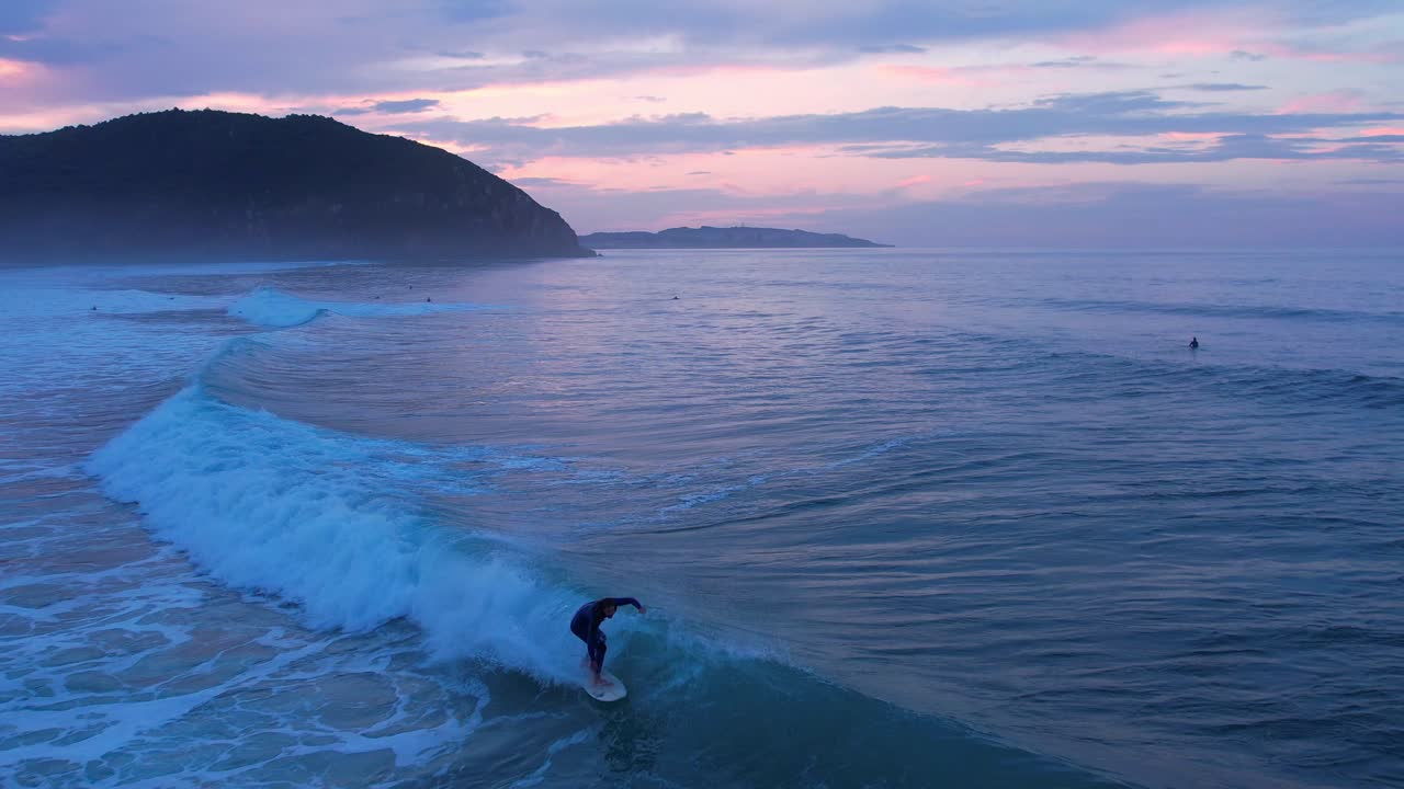석양에 스페인 칸타브리아의 베리아 해변에서 파도를 타는 서퍼의 드론 샷