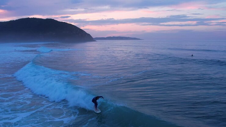 Drone shot of a surfer riding the wave at Berria beach in Cantabrian, Spain at the sunset