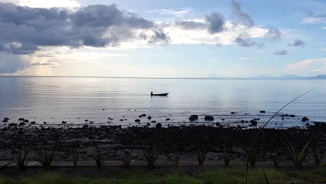 A-local-fishermen-paddling-a-small-traditional-wooden-fishing-canoe-in-the-shallow-water-at-low-tide-in-early-morning-sunrise-light