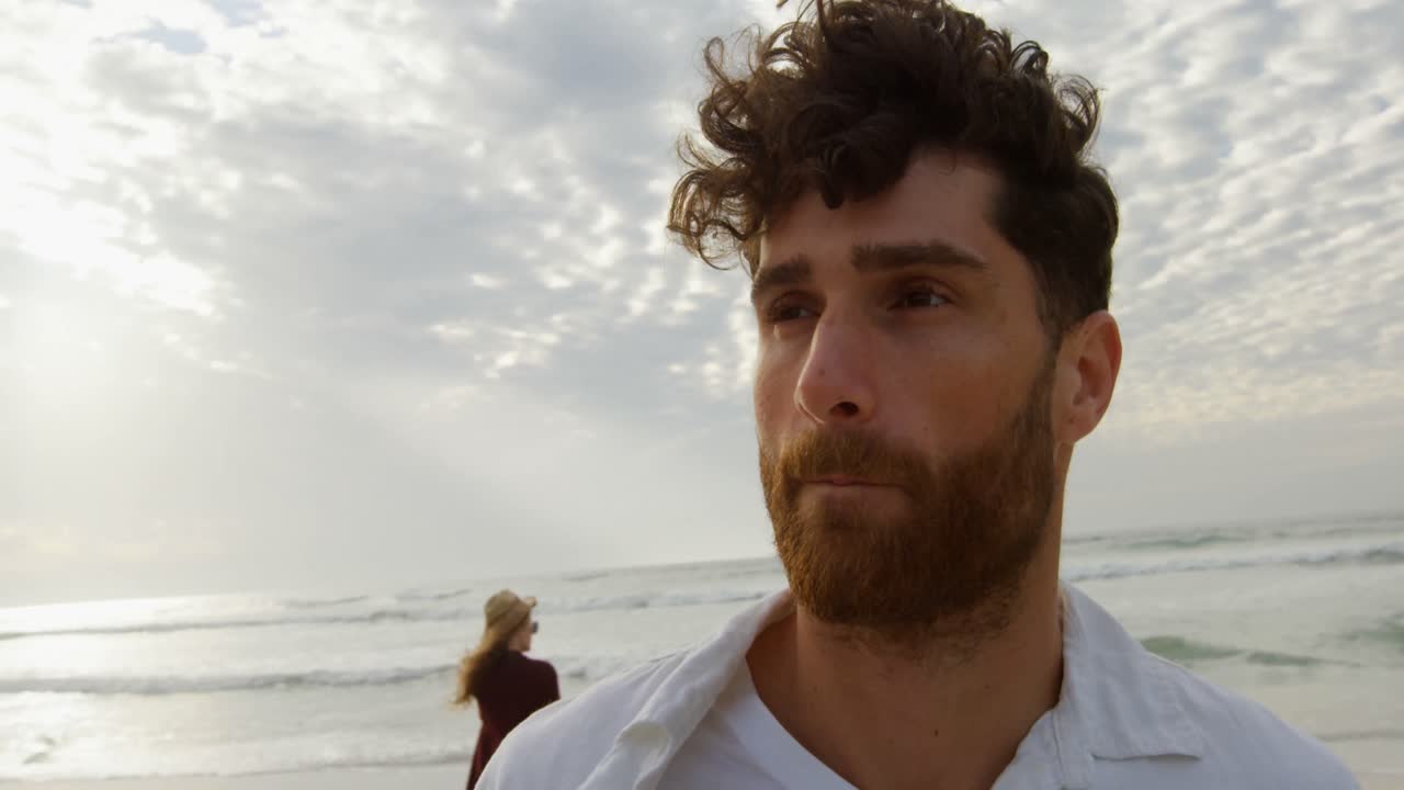 Vista frontal de jovem homem caucasiano de pé na praia em um dia ensolarado 4k