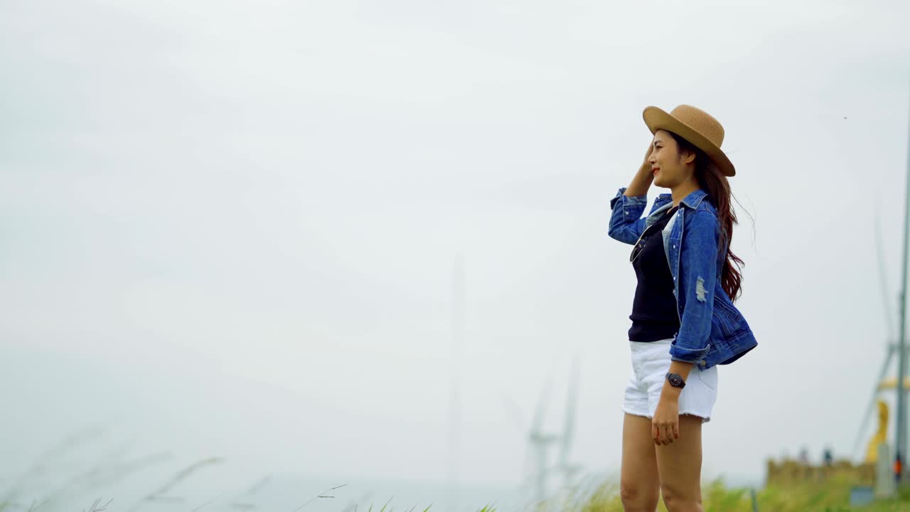 아시아 여성들이 산 위에 행복하게 서 있습니다. 풍차의 배경이 있습니다.