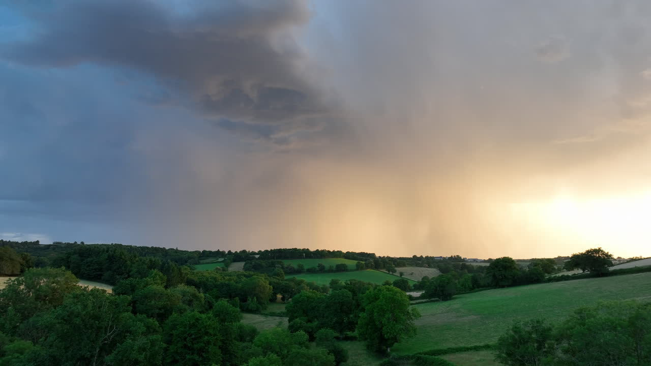 Aerial flying over rural Saint-Maigner at sunset, rain falling in background, France