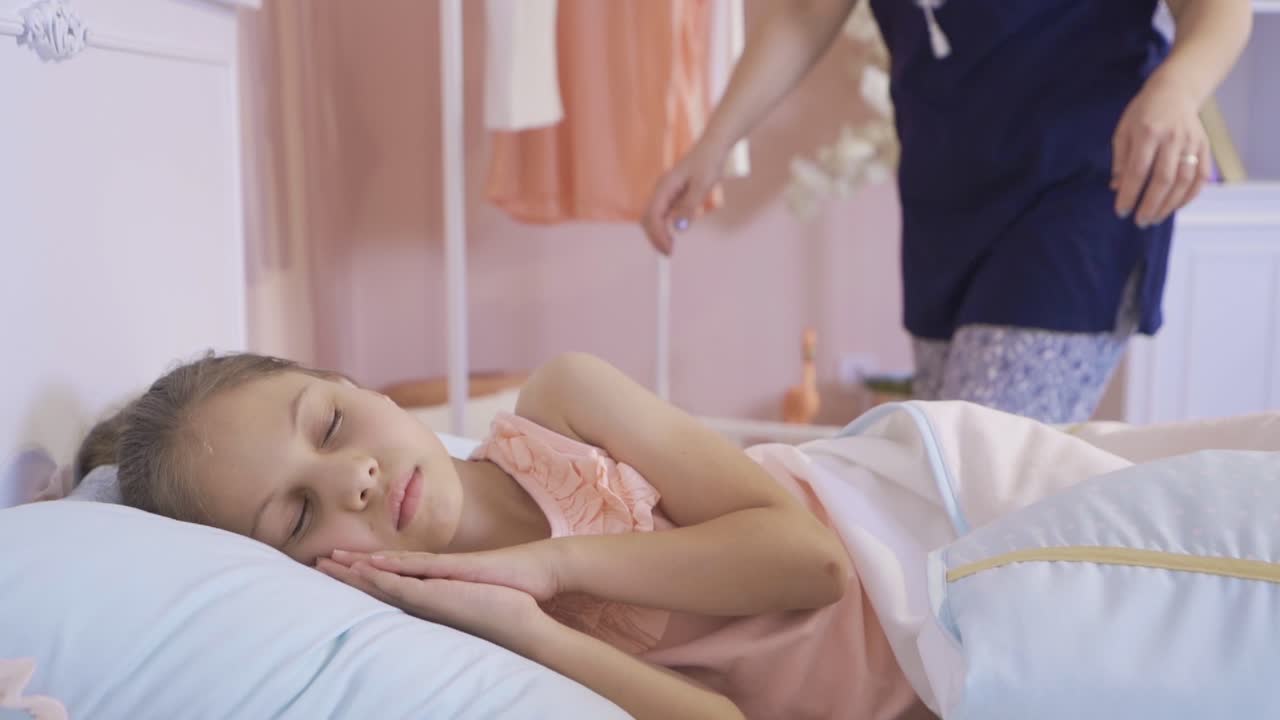 The mother, straightening her daughter's blanket, kisses her cheek.