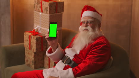 Santa-Señala-Con-El-Dedo-La-Pantalla-Verde-Del-Teléfono-Móvil.-Venta-De-Navidad.-El-Anciano-Papá-Noel-Muestra-Una-Pantalla-Con-Un-Cromakey.-Imágenes-4k-De-Alta-Calidad