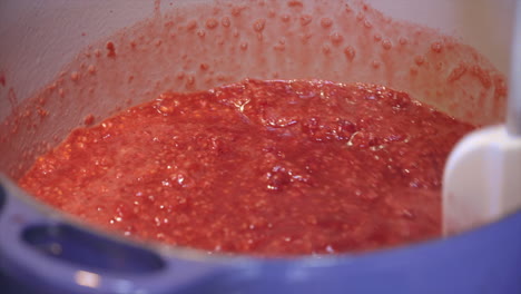 puré de frambuesa rojo brillante revuelto en una olla azul, cerrar