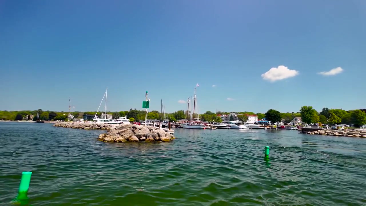En naturskøn båd sejler fra Sister Bay Marina, passerer fortøjede fartøjer og havnens stenmole, før den sejler ud i det åbne vand i Green Bay, Wisconsin.