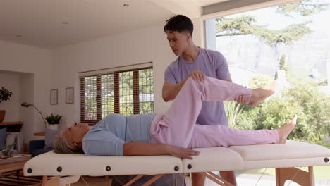 physiotherapist assisting senior woman with leg exercises on therapy table indoors