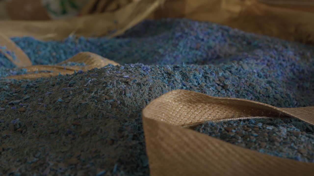 Jemné modré drcené plastové vločky shromážděné uvnitř otevřeného velkoobjemového vaku v recyklačním zařízení