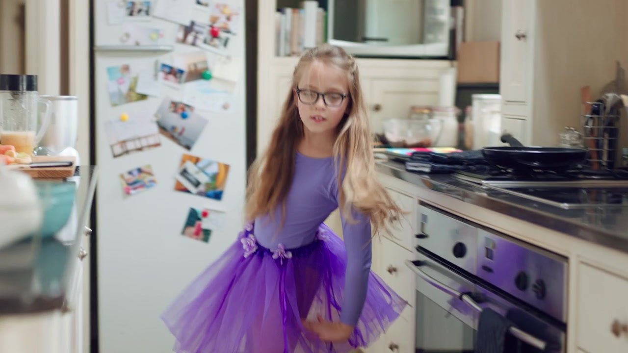 Bambina che balla con un tutù viola in cucina