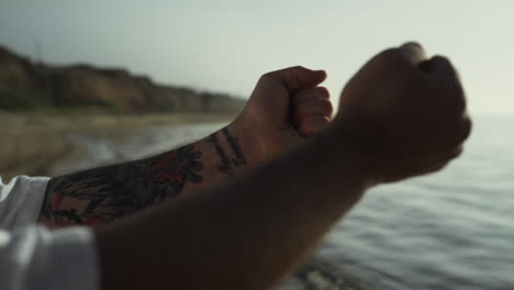 manos de hombre tatuadas haciendo calentamiento al atardecer de cerca. ejercicio en la naturaleza de verano.