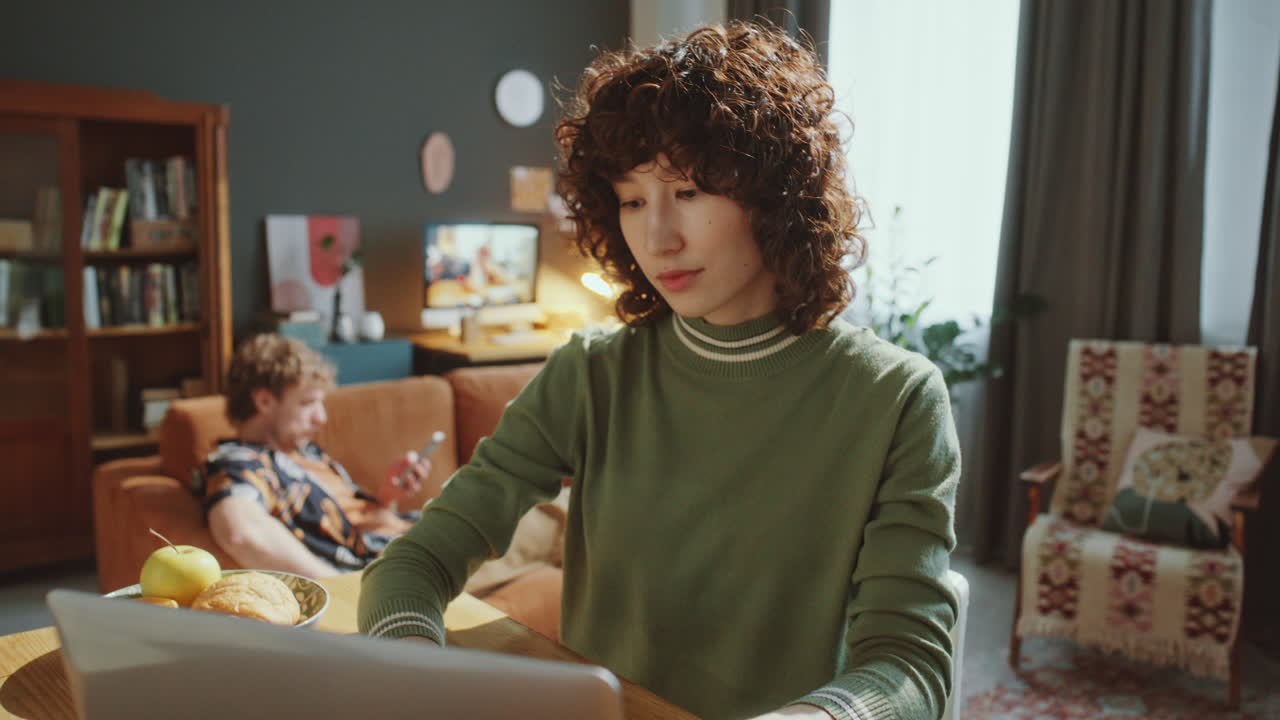 Young Asian Woman Using Laptop at Kitchen Table during Day at Home