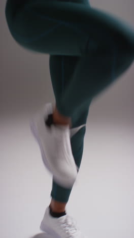 vertical video close up shot of female athlete wearing tracksuit training in gym fitness class running on the spot against plain background in real time