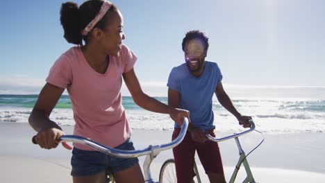 african american couple smiling and riding bikes on the beach