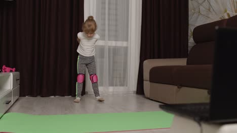 Girl-kid-girl-doing-gymnastics-stretching-workout-at-home,-watching-online-lessons-on-laptop-pc