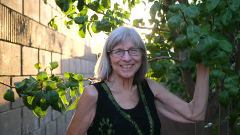 An-elderly-woman-smiling-with-joy-clipping-branches-and-pruning-a-pear-fruit-tree-in-her-orchard-garden-at-sunset