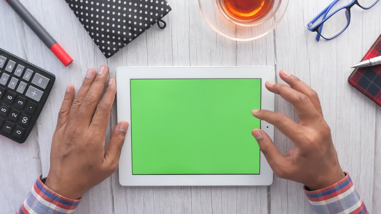 Person using a tablet with a green screen on a wooden desk
